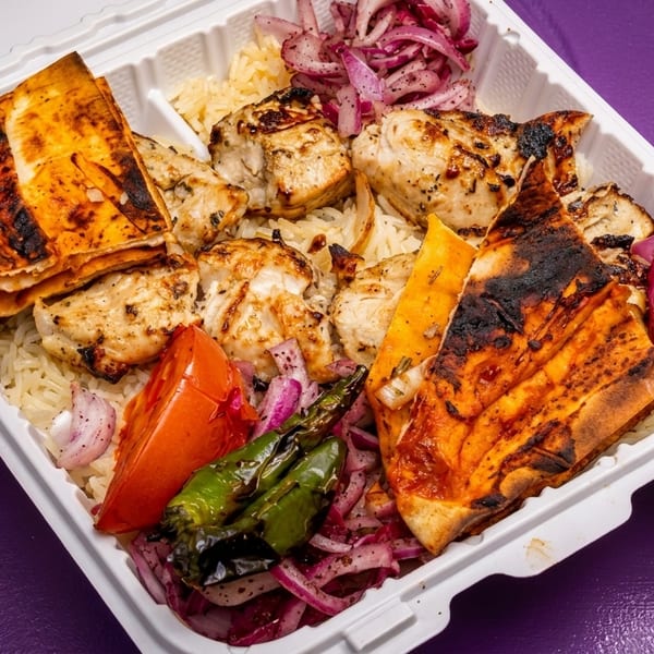 Grilled chicken, rice, red onions, tomatoes, and peppers in a white takeout container.