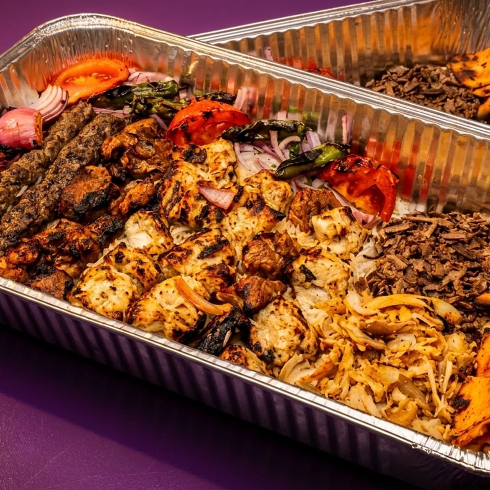 Two foil trays filled with various grilled meats, rice, vegetables, and pita bread.
