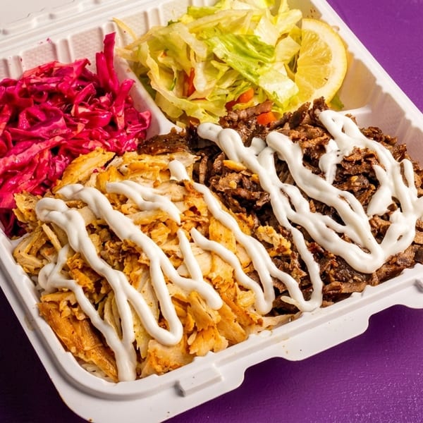 Takeout container with chicken and beef shawarma, red cabbage, lettuce, and a lemon wedge.